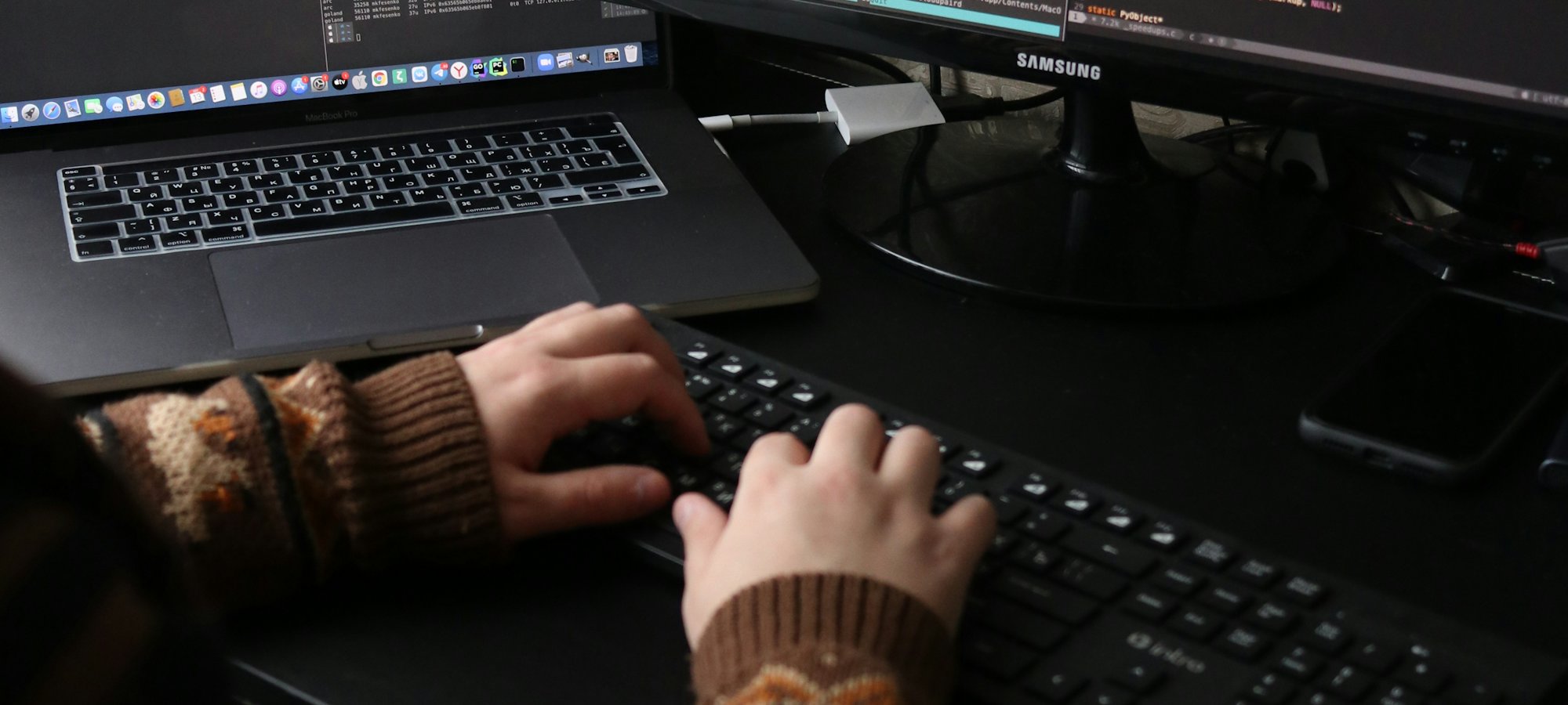 Handen op een toetsenbord voor twee schermen met programmacode